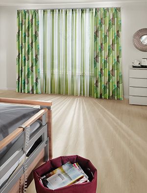 Wohnraum mit grün gemusterten Vorhängen aus der Serie Elegante Erscheinung und heller Holzoptik