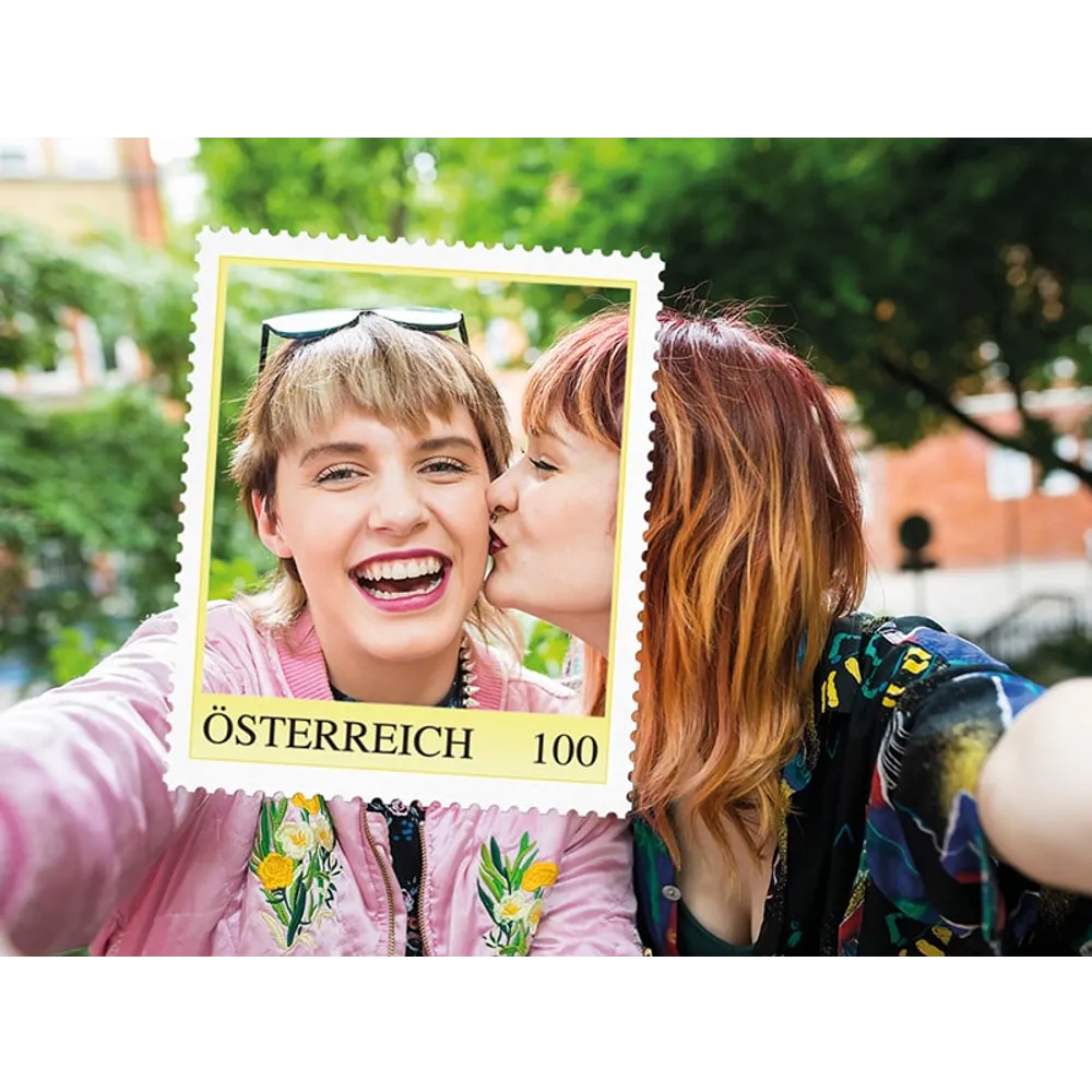 Zwei Frauen posieren mit einem Rahmen in Form einer Briefmarke der Österreichischen Post, beschriftet mit 'Österreich 100'.