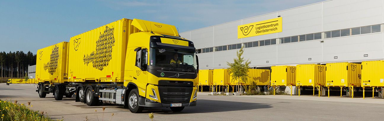 Logistikzentrum der Österreichischen Post in Oberösterreich mit gelbem Post-Lkw und Containern vor dem Gebäude.